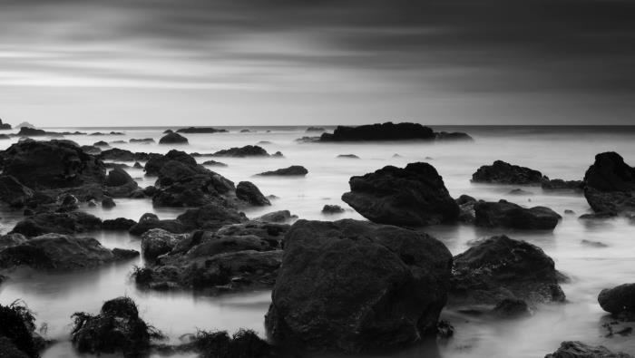 svartvitt fotografering av en stenig strand i dimman, ett havslandskap genomsyrat av en viss mystik