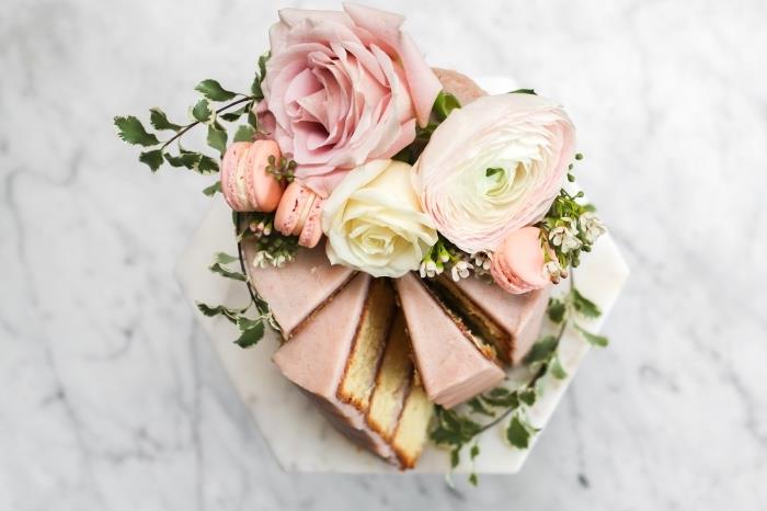 čo domáci dezert na romantické jedlo navrchu, okrúhly model cupcake s pastelovo ružovou polevou ozdobený makrónkami a čerstvými kvetmi