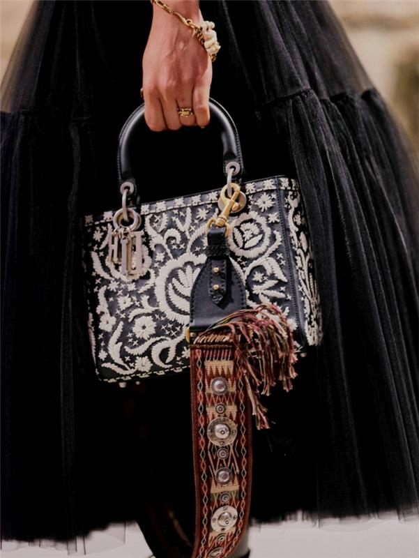 lång svart kjol, texturerad väska med blommiga figurer, guldarmband, svart statementhandtag