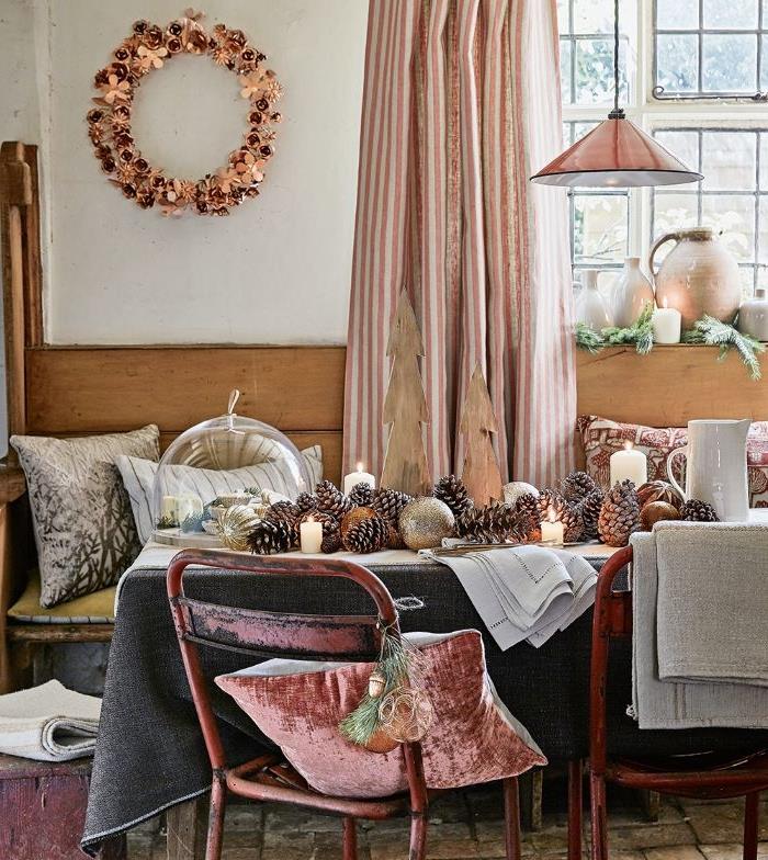 rustikálna jedáleň so stolom zdobeným stredobodom sivého obrusu, borovicovou šiškou a kovovými sviečkami a dekoračnými vankúšmi z drevenej lavice