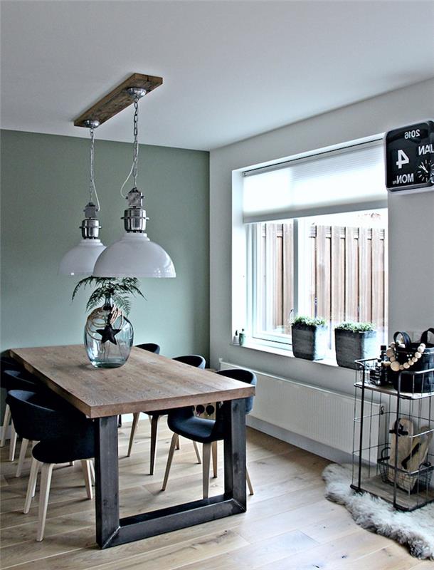 Zelená jedáleň Celadon, drevený a čierny kovový stôl, čierne škandinávske stoličky, svetlé parkety, zelené rastliny a závesné svetlá v industriálnom štýle