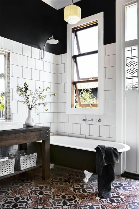 svartvitt badrumsinredning, svartvitt badkar i gjutjärn, vita kakelplattor och cementgolv; svarta väggar
