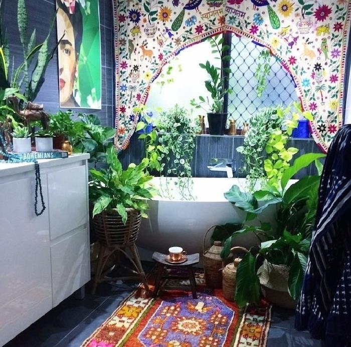 rám na stenu deida frida khalo, orientálny koberec na sivej dlažbe, biela kúpeľňová skrinka, niekoľko rastlín okolo vane, orientálny textilný panel s potlačou