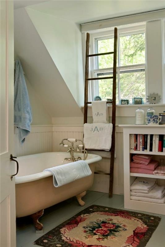 malý koberec s kvetinovými motívmi, pastelová vaňa, chrómový faucet, drevený rebrík, malá úložná jednotka s knihami a uterákmi