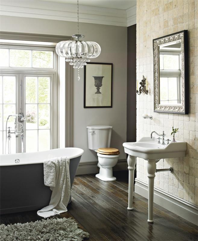 kristall taklampa, stort badkar i grått och vitt, vintage vitt handfat, mörkt parkettgolv, rektangulär inramad spegel, imponerande badrum
