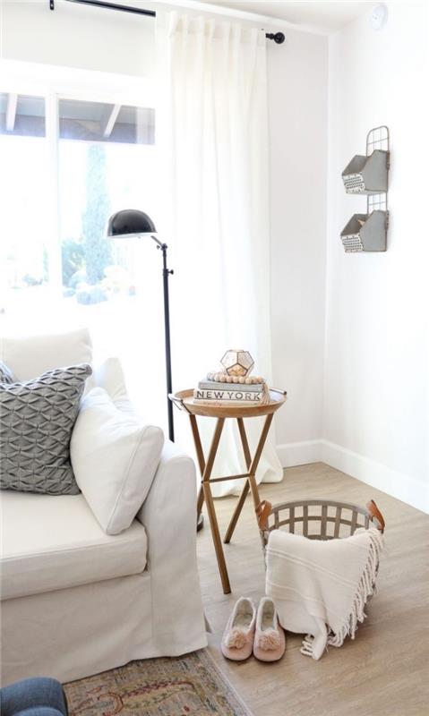 sittgrupp i vitt vardagsrum i skandinavisk stil med en vit soffa dekorerad med en grå texturerad mönsterdyna, ett sidobord i vintage design och en förvaringskorg