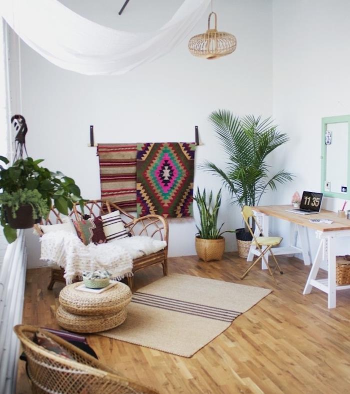 bohémska elegantná moderná obývacia izba so stolom, ratanovým kreslom s bielym plédom, svetlými parketami, zelenými rastlinami a kobercom na stenu