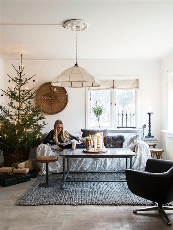 dekor vardagsrum med en skandinavisk och traditionell festlig stämning, en relaxavdelning i vardagsrummet med en liten soffa med grå fuskpälskuddar och en julgran placerad vid sidan