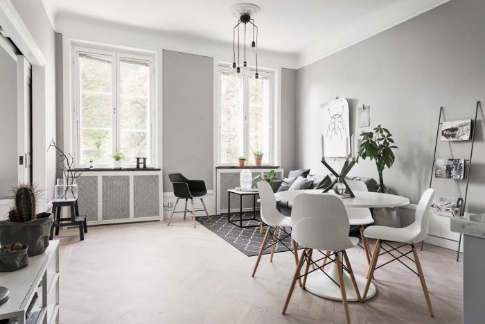 sivá a biela výzdoba obývačky, perleťovo šedá stena, jedálenský kút s bielym stolom a škandinávskymi stoličkami, sivá sedačka a geometrický škandinávsky koberec, sivobiely škandinávsky nábytok