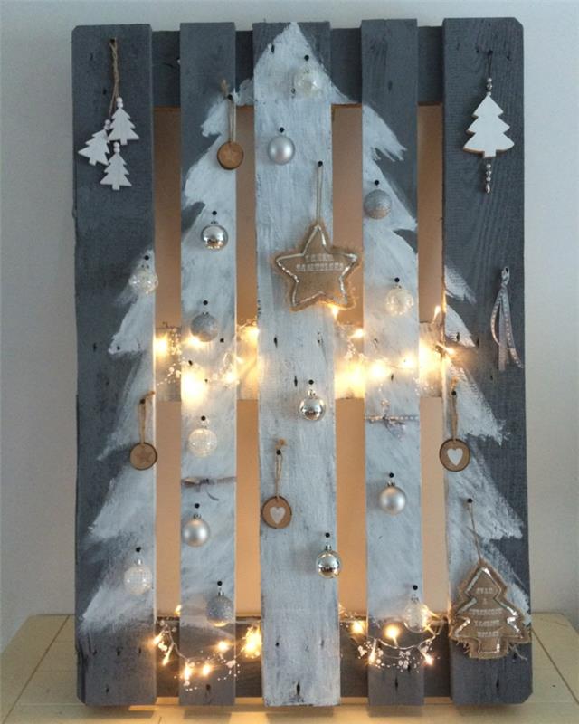biely vianočný stromček namaľovaný na palete, malé ozdobné stromčeky, ozdoby na vianočné stromčeky zavesené na paletových doskách