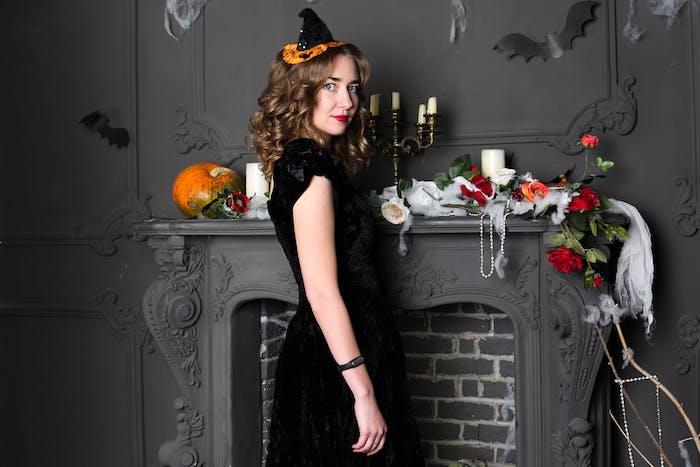 trollkarlskostym, häxstil med en svart klänning och en original häxmössa i svart och orange, halloween eldstad dekor