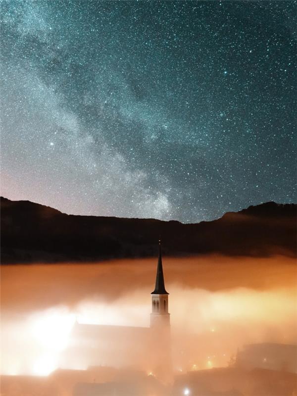 Faro in mezzo alla nuvole, cielo sereno con stelle, città con nuvole