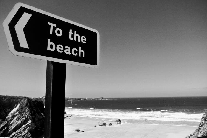 svartvitt foto av ett riktningsskylt och den öde stranden i bakgrunden, svartvit fotografering