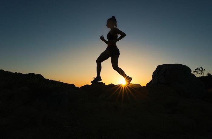 silhuett av en kvinna framför solen som springer över stenar