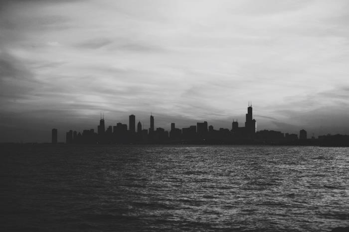 svartvitt silhuettbild av en stad som hägrar vid horisonten bakom det lugna vattnet i havet