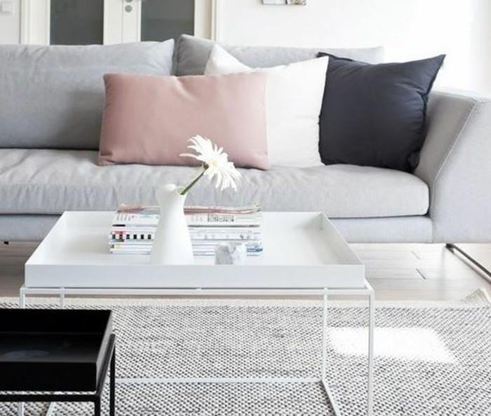 Tavolino basso di colore bianco, divano con cuscini colorati, salotto con tappeto grigio