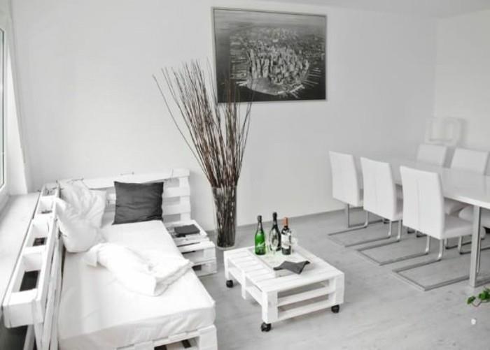 Open space arredato con un divano in pallet di colore bianco, tavolino basso con rotelle