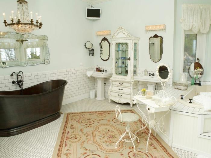 stort svart badkar, stor viktoriansk ljuskrona, dekorativ spegel, beige matta, liten pall och vitt bord, två handfat, vintage skänk