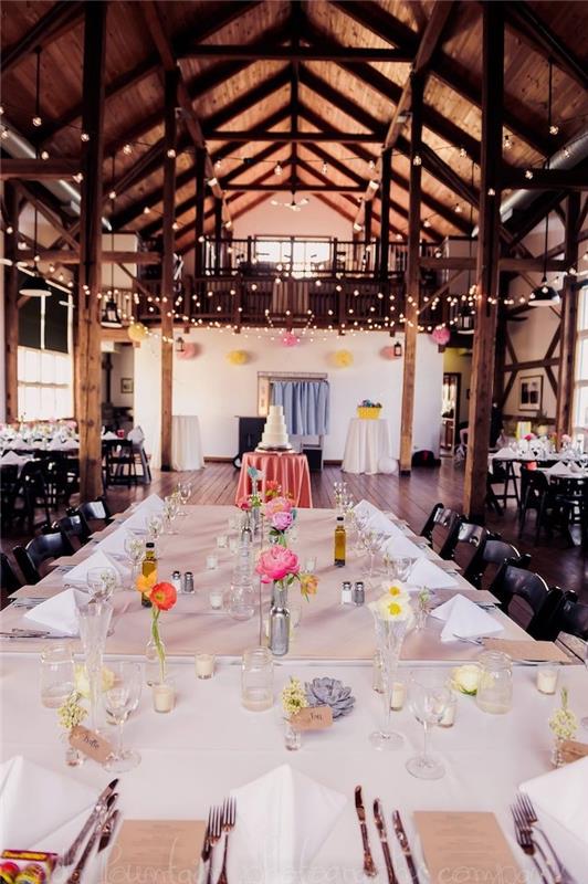 výzdoba svadobného stola v malých soliflorách na bielom obruse, svetlá girlanda na ozdobenie zalesneného stropu odhalenými trámami