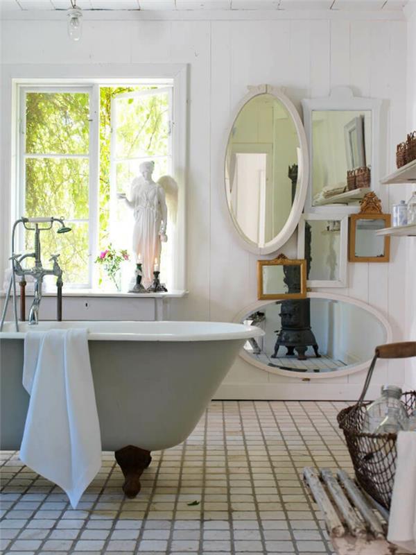 antikt badrum, vit oval spegel, stort centralt badkar, vitt klinkergolv, rustik spis, vit panel