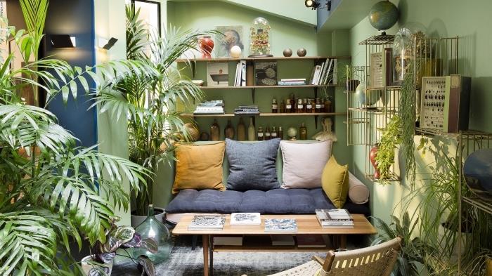 nápad na etnickú výzdobu v malej obývačke so zelenými stenami so zelenými rastlinami, model nízkej pohovky pokrytý vankúšmi