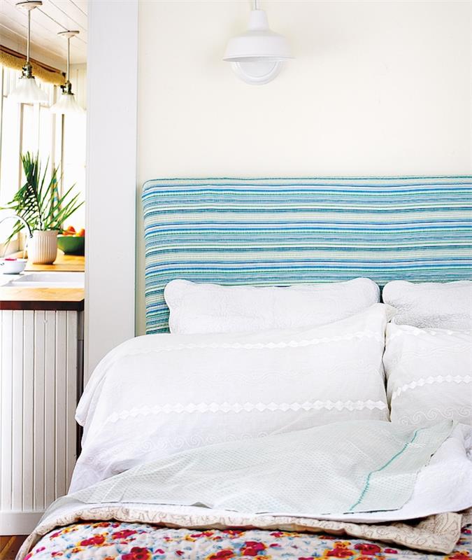 design sänggavel med blå och vita ränder, vita sängkläder och rabatter i ett öppet sovrum