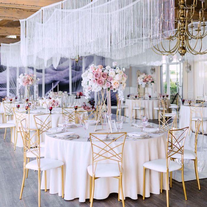 ozdobte svadobný strop jesennou výzdobou z bielych nití nad stolmi v bielych obrusoch obklopených zlatými a bielymi stoličkami elegantnými kyticami kvetov