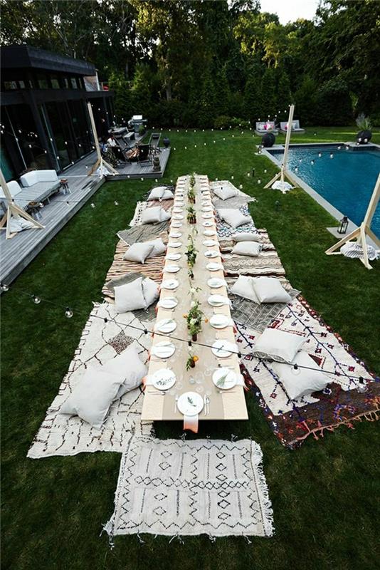 picknick-bord-grön-gräsmatta-ett-stort-trä-bord-vita-kuddar-idé