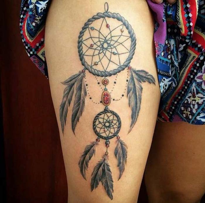exempel på en dreamcatcher -tatuering på låret, rephylsa, nät och grå fjädrar, stenar och färgade pärlor