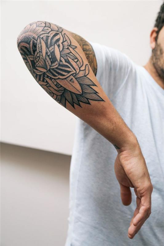 mužské tetovanie kompasom, vytetovaná polovičná ruka, biele tričko, symboly vytetované na lakte