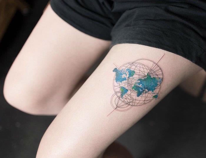 وشم خريطة العالم planisphere بألوان مائية زرقاء وخضراء ودوائر هندسية مجردة على فخذ الأنثى