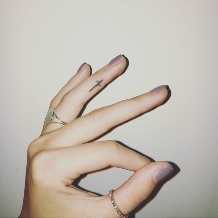 en nästan omärklig handtatuering, litet kors tatuerat på sidan av fingret