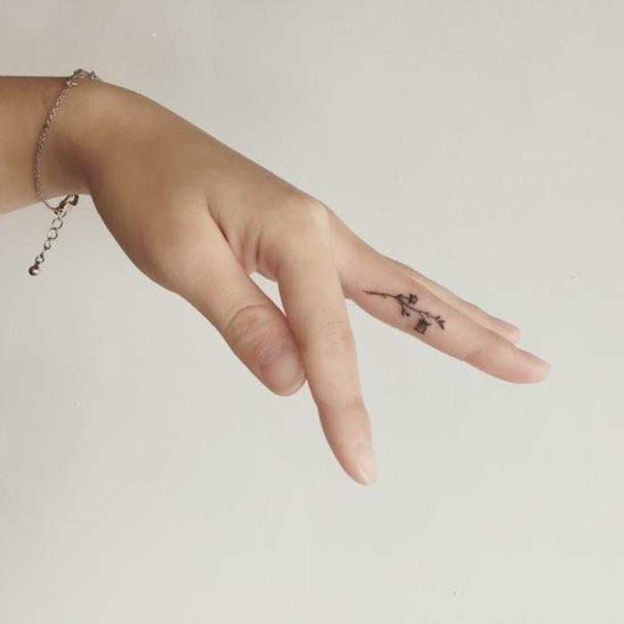 en minimalistisk tatuering på fingret med ett blommönster, subtil och feminin tatuering