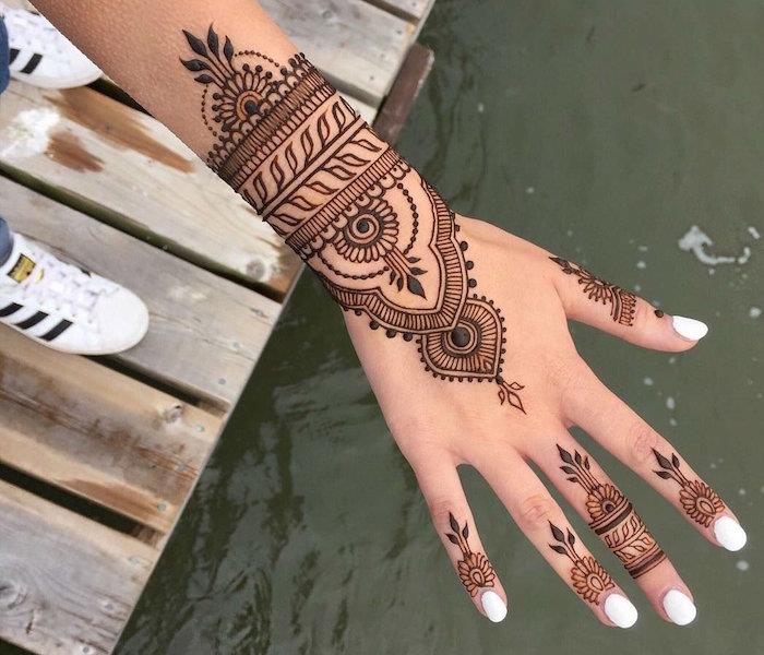 يد بتصميم الحناء على الأصابع وسوار من الدانتيل على غرار المعصم مع أظافر بيضاء ونجم أديداس