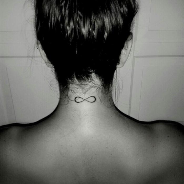 liten diskret infinity -tatuering på kvinnans baksida