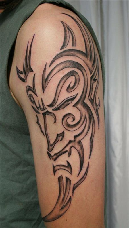 tetovaná maska ​​muža na ruke, totemové tetovanie čiernej farby, tetovanie na ramene
