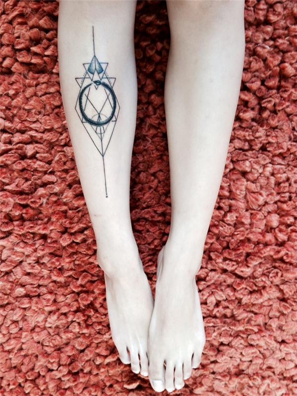 symbolické vertikálne tetovanie s geometrickým tvarom a ouroborosom zvnútra urobeným na nohe