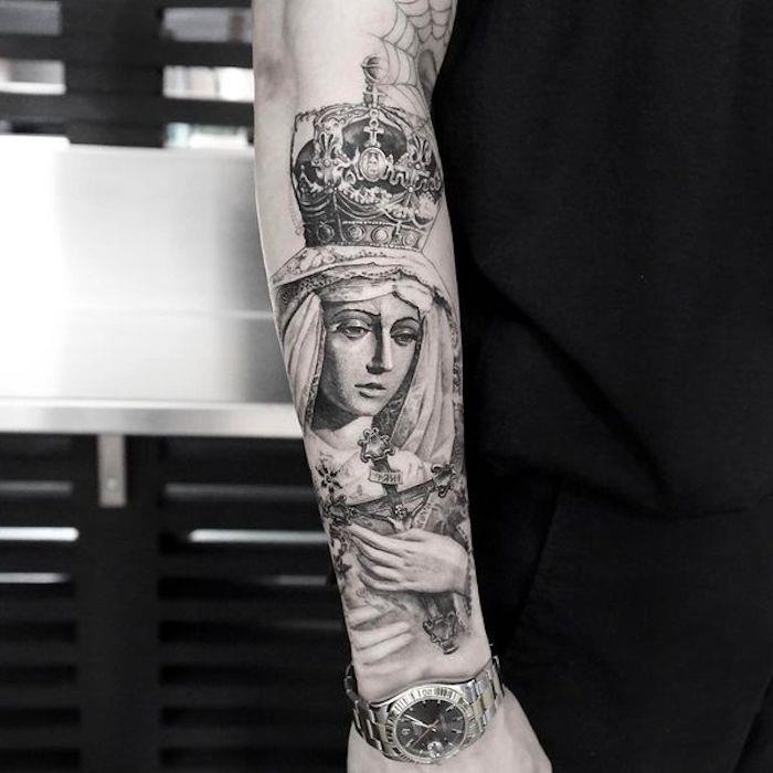 Il braccio di un uomo con un grande tattoo religioso con donna e croce in mano