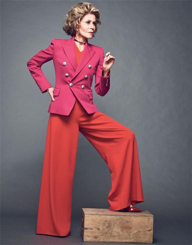 outfit med utsvängda byxor och röd topp och en rosa jacka lockigt hår frisyr kvinna 60 år vågigt torg
