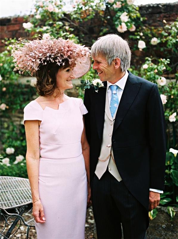 bröllopsklänningidé för kvinna 60 år för brudens mor, rosa klänning med rakt snitt och kort ärm med asymmetrisk urringning, åtföljd av en bröllopshatt av samma färg