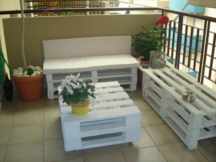 Balcone con ringhiera in ferro battuto, arredamento con bancali, divano e un tavolino