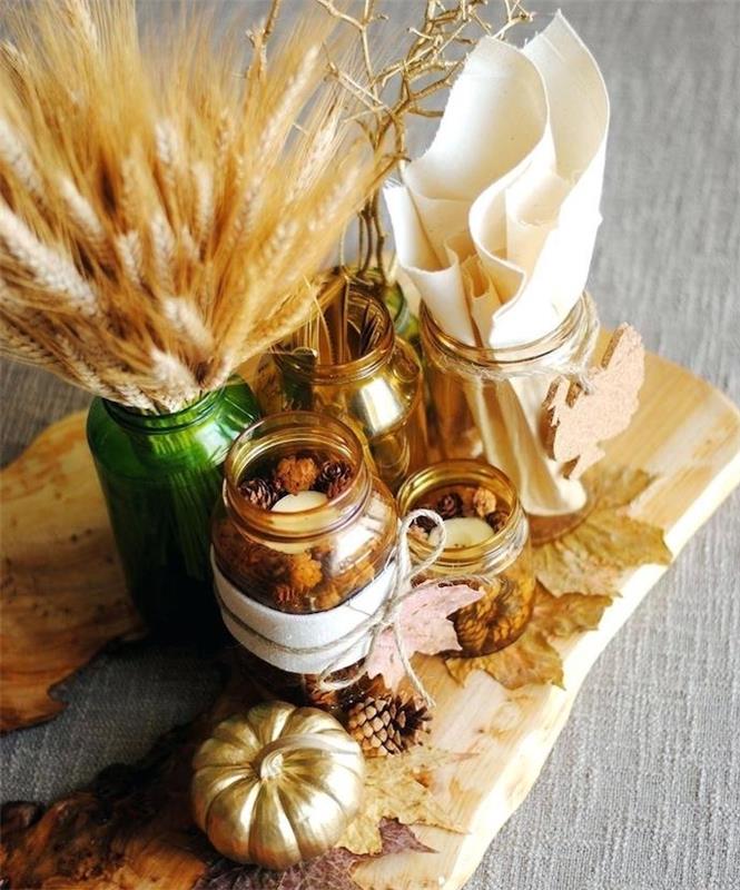 زخرفة طاولة الخريف ، قطعة مركزية من الألواح الخشبية مع مرطبانات زجاجية مملوءة بأقماع الصنوبر ، إناء بأذن من القمح والقرع الذهبي