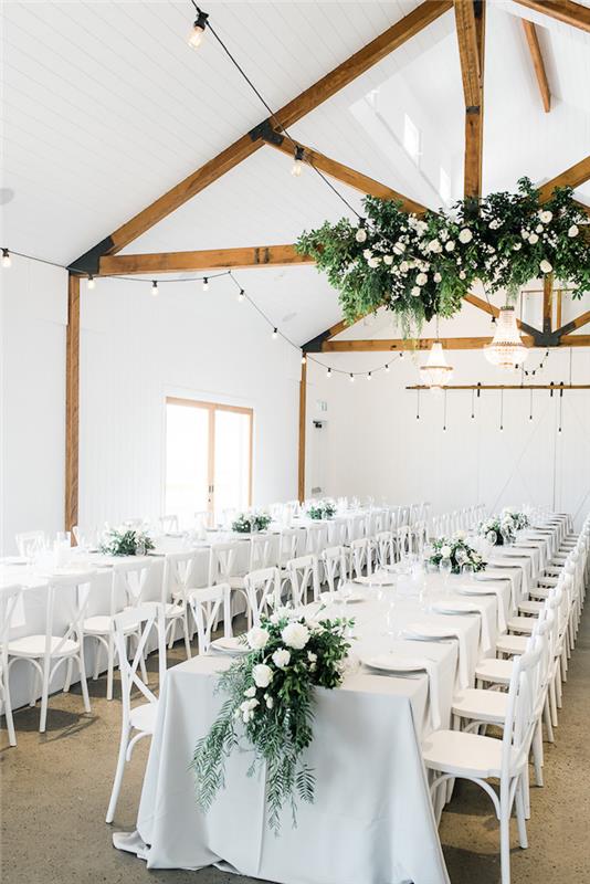 výzdoba svadobnej miestnosti v bielej farbe so zelenou vegetáciou a bielymi kvetmi, odhalené trámy v svadobnej miestnosti, zavesená vegetácia