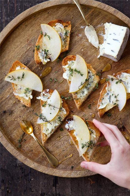 klasický recept na aperitívový toast s rokfortom, hruškami a čerstvým tymianom podávaný na drevenej doske so syrom, nápad na párty toastový aperitív
