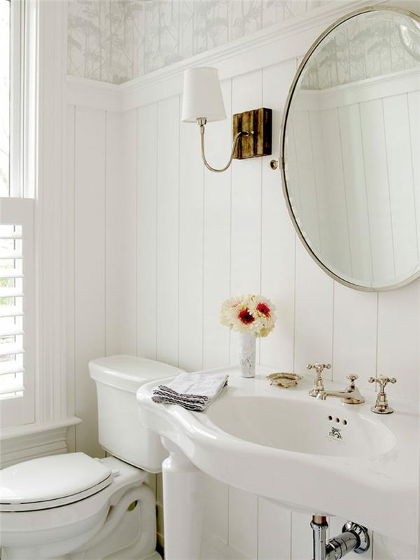 pekná wc dekorácia v bielej farbe, okrúhle zrkadlo, vintage štvornohé umývadlo, biele obloženie steny, retro vodovodné batérie