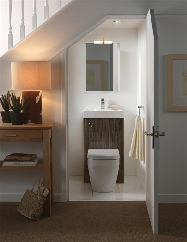 toaleta pod drevenými a bielymi schodiskami, biela farba na WC, malá skrinka pod umývadlo