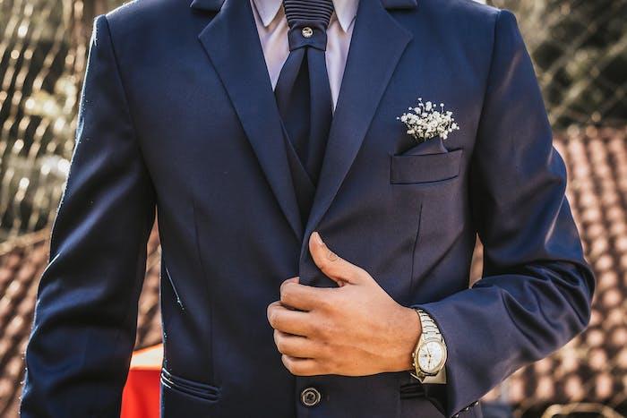 muž oblečený v modrom obleku s kravatou a hodinkami okolo rúčky