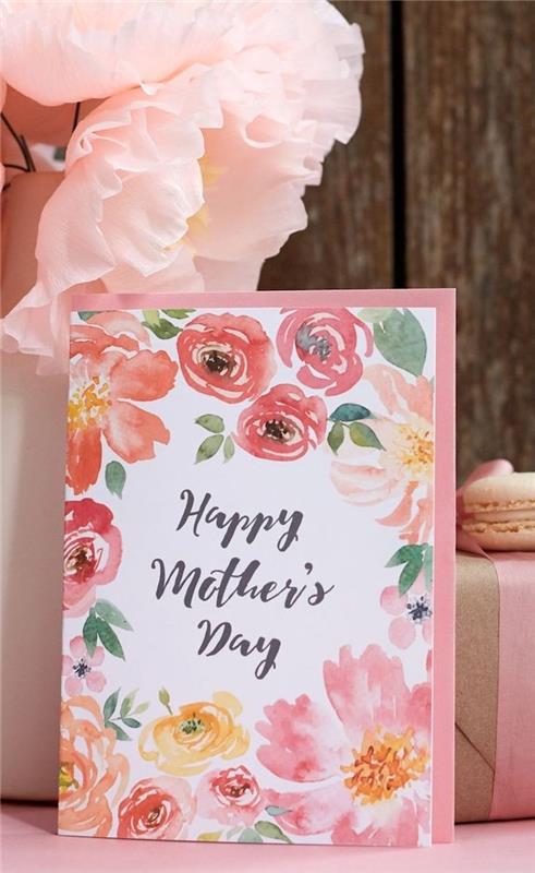 kartička v ružových odtieňoch vedľa umelých kvetov a makrónky