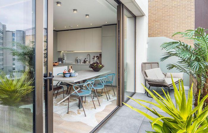 kök som vetter mot en terrass täckt med betong, med palmer, succulenter, rottingstol, grå kuddar