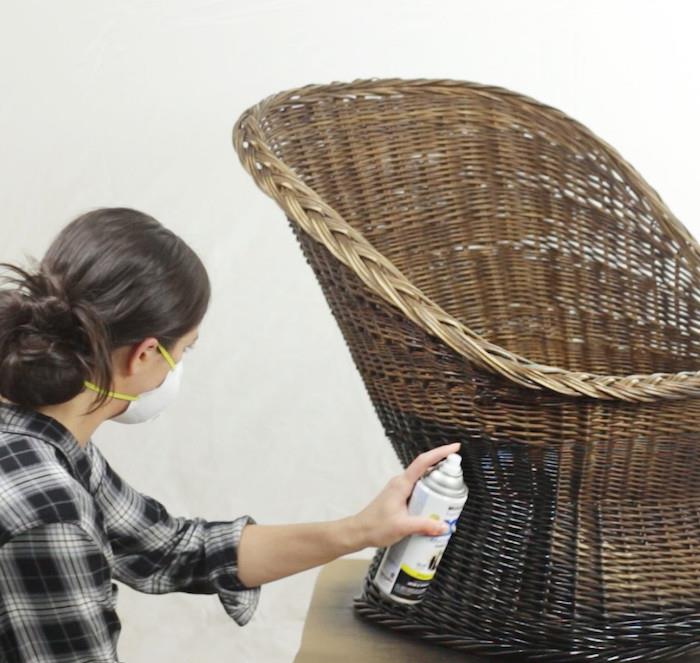 kvinna med mask målar rottingstol med sprayfärg